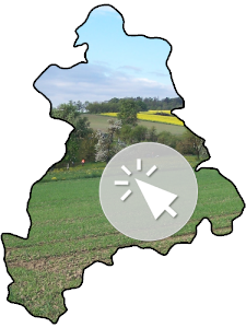 Die Landkreissilhouette, gefüllt mit einem Foto eines grünen Ackers und einem Pfeil im Kreis, der anzeigen soll, dass das Bild mit einem Link zum entsprechenden BürgerGIS-Projekt hinterlegt ist.